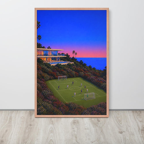 A framed vertical abstract football wall art print depicting a soccer field at dusk with a modern house, ocean, and colorful sky, displayed against a light gray wall on a light wood floor.