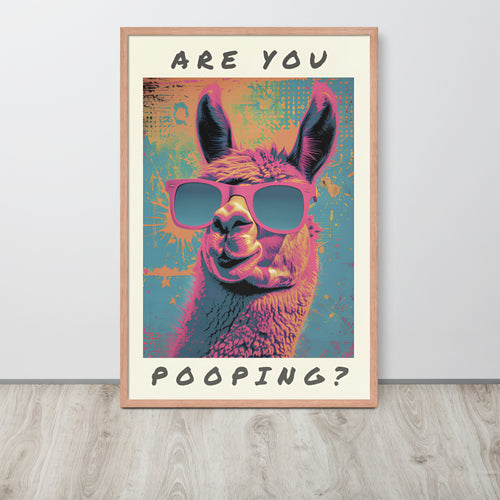 Whimsical washroom wall art leaning against a light wall on a wood floor. The poster shows an alpaca wearing pink sunglasses with the text 'ARE YOU POOPING?' in black at the top and bottom.
