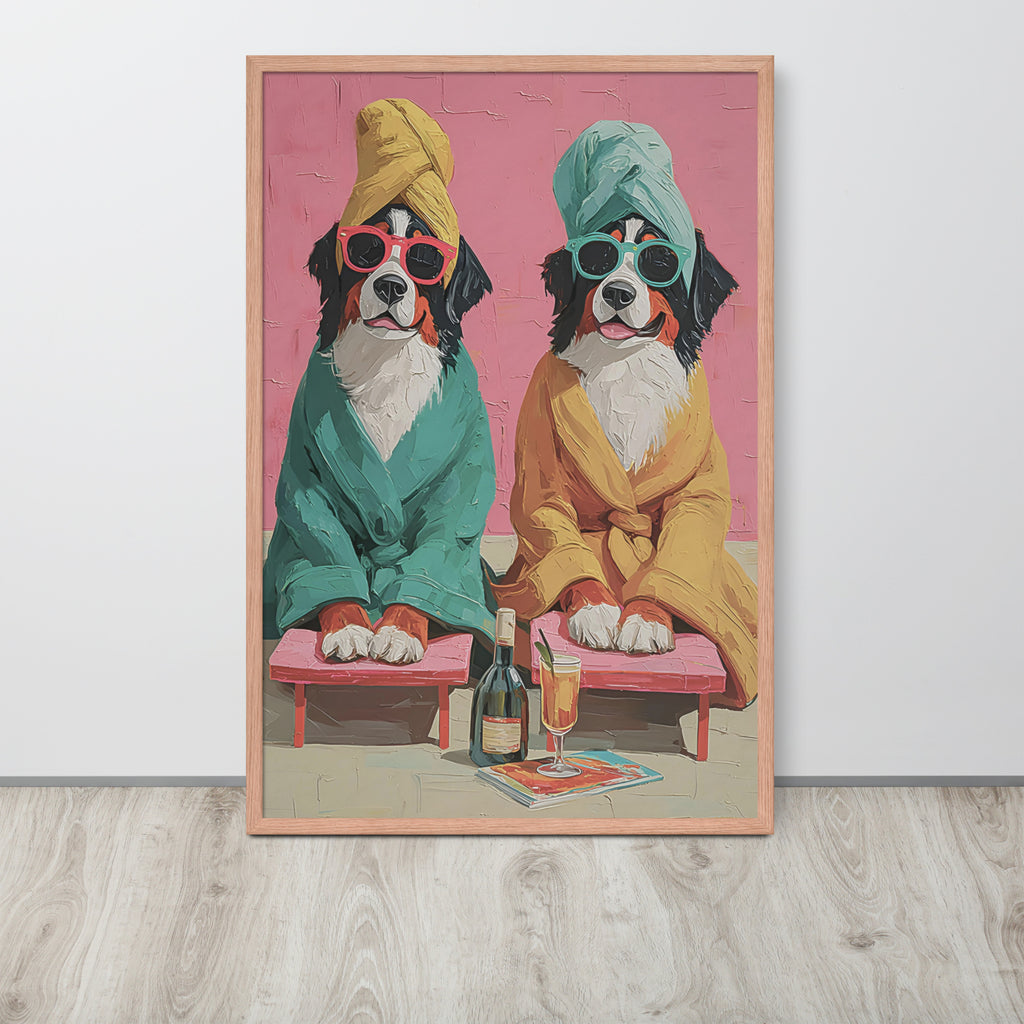 Whimsical bathroom wall art print leaning against a white wall on a light wood floor. The print shows two Bernese mountain dogs dressed in colourful robes and towels, sitting on pink chaise lounges with a bottle and glass in front of a pink background.