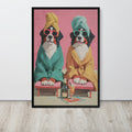 Funny dog bathroom art print depicting two Bernese mountain dogs dressed in bathrobes and towels, sitting on pink chaise lounges with a bottle and glass in front, displayed on a light wood floor against a white wall.