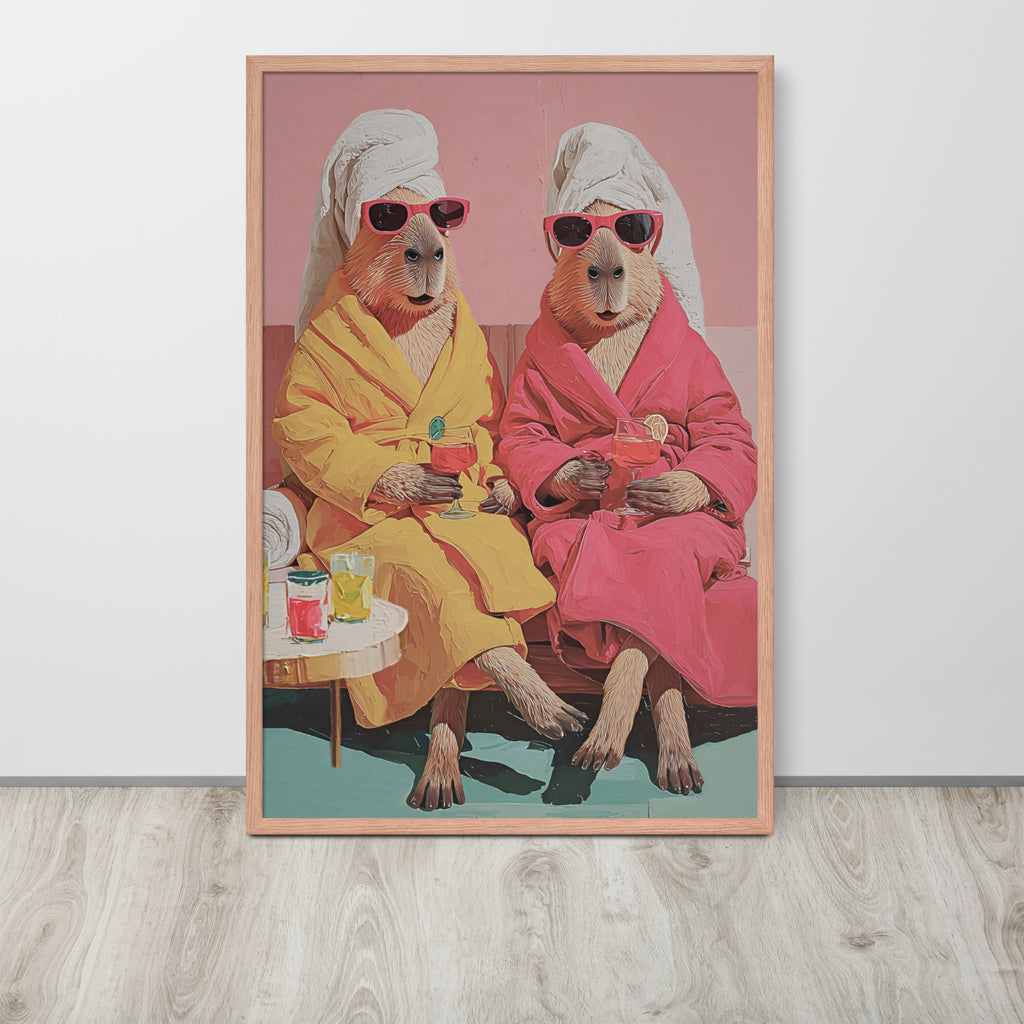 Funny capybara bathroom wall art print featuring a retro-style illustration of two anthropomorphic capybaras in pink and yellow robes wearing sunglasses and holding cocktails, displayed on a light wood floor against a white wall.