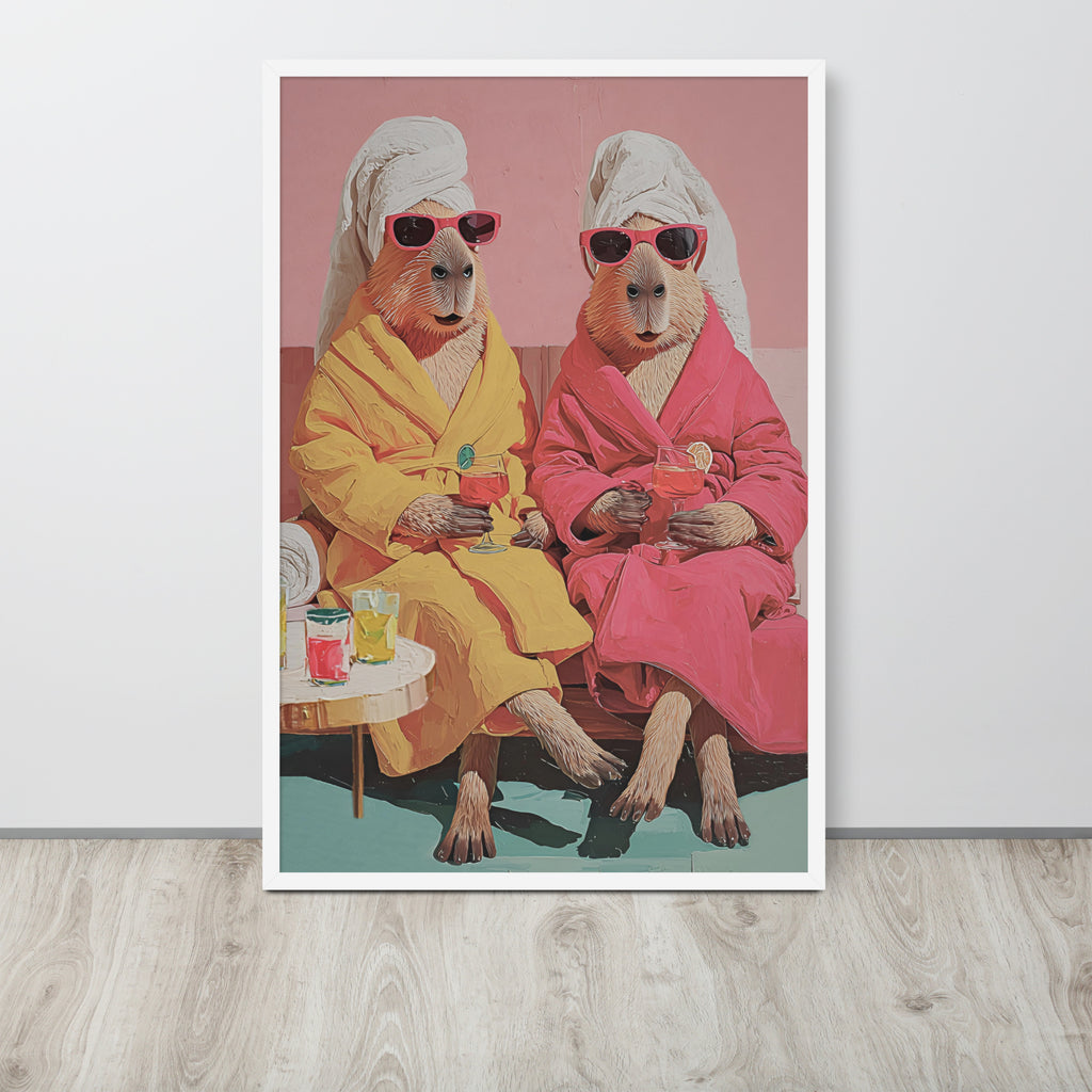 Whimsical capybara wall art poster print featuring a stylized illustration of two anthropomorphic capybaras in pink and yellow robes wearing white towels and sunglasses, sitting on a bench against a pink background. The print is displayed leaning against a light gray wall on a light wood floor.
