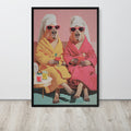 Capybara wall art print featuring a stylized illustration of two anthropomorphic capybaras in pink and yellow robes wearing white towels and sunglasses, sitting on a bench against a pink background. The print is displayed on a light gray wall above a light wood floor.