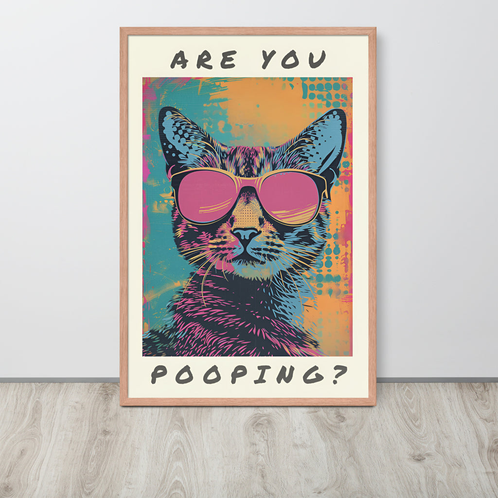 Funny cat toilet pop-art style poster leaning against a light wall on a wood floor. The artwork shows a cat wearing pink sunglasses with the text 'ARE YOU POOPING?' in black at the top and bottom.