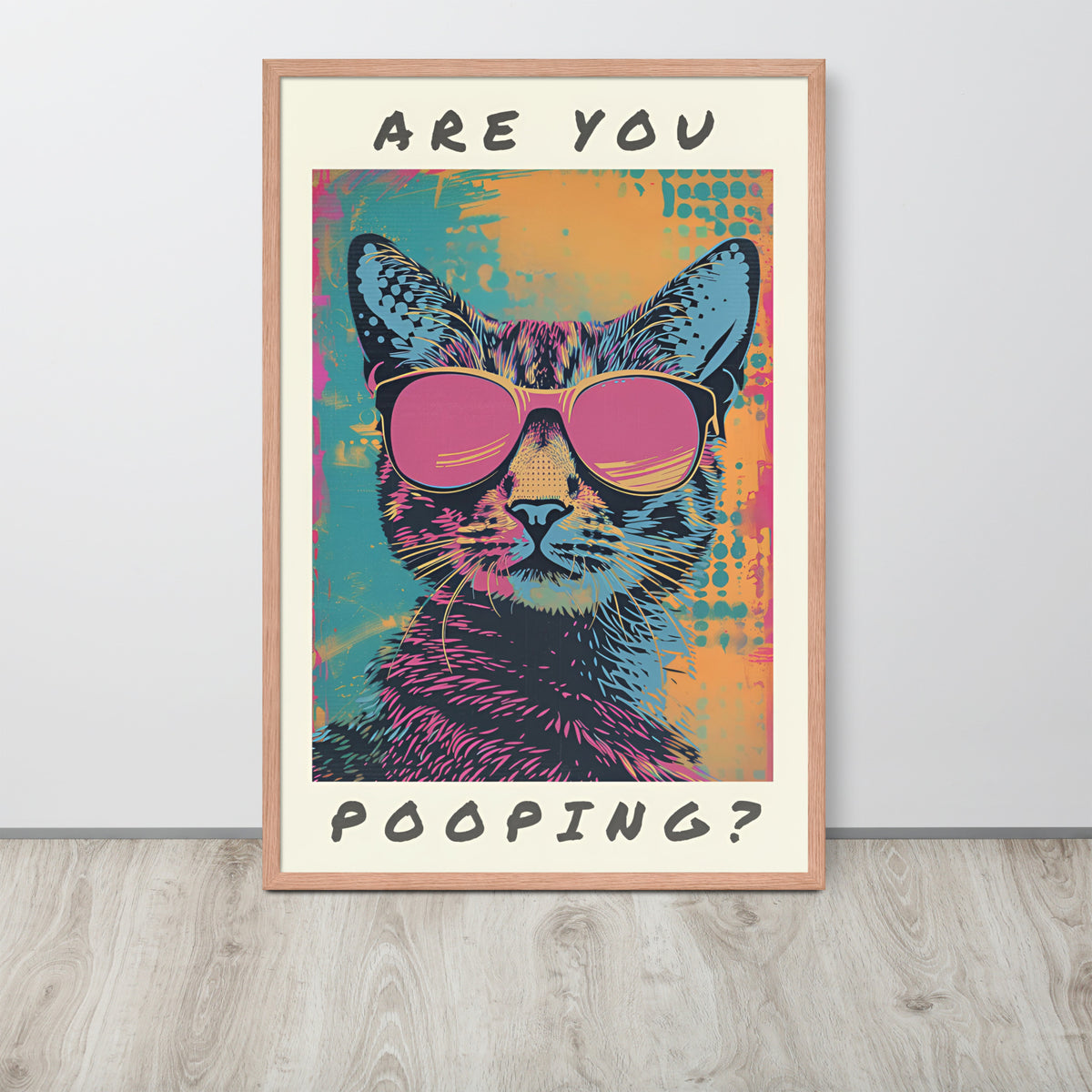 Funny cat toilet pop-art style poster leaning against a light wall on a wood floor. The artwork shows a cat wearing pink sunglasses with the text 'ARE YOU POOPING?' in black at the top and bottom.