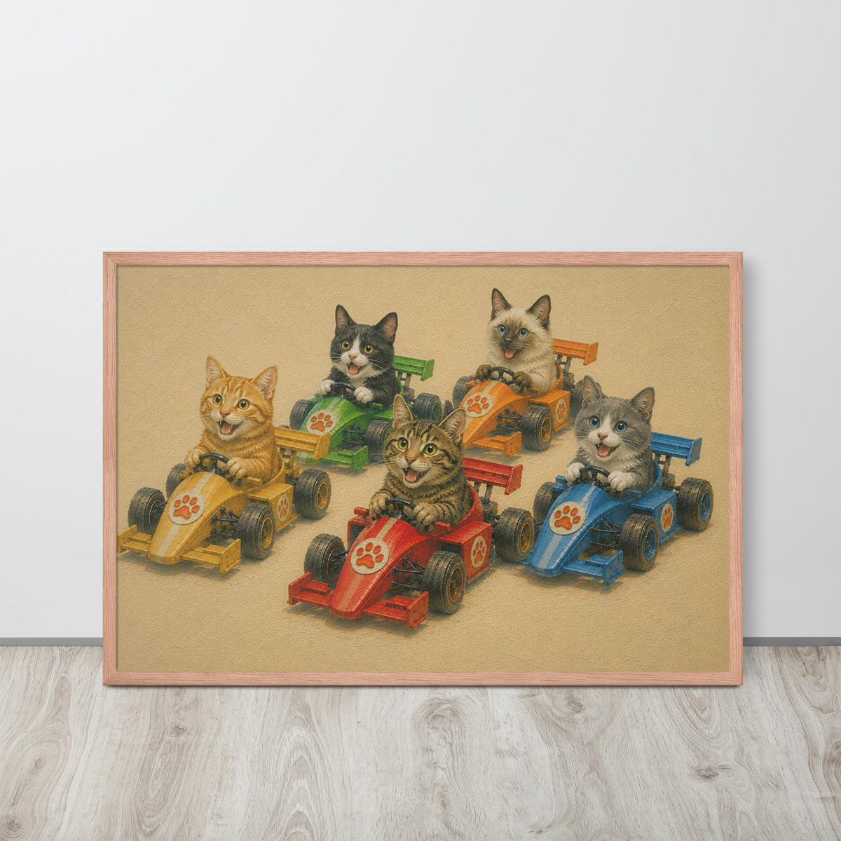 A framed cat nursery wall art print featuring five cats driving colourful race cars, displayed on a light wood floor against a white wall.