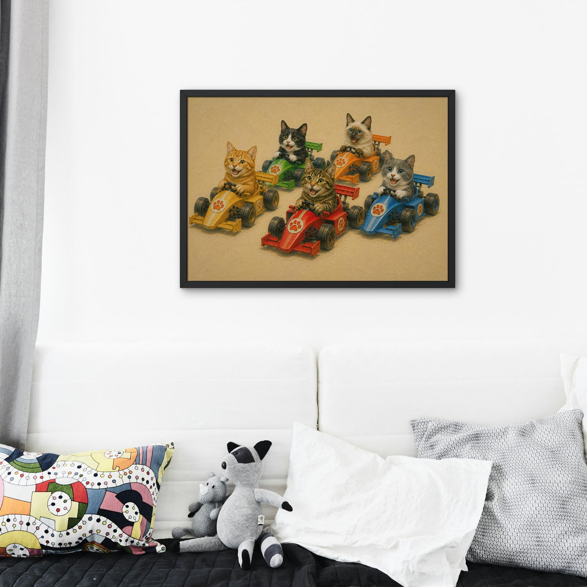 A framed F1 nursery wall art poster print depicting five cats racing in toy formula one race cars, displayed on a white wall above a couch with pillows and a plush toy.