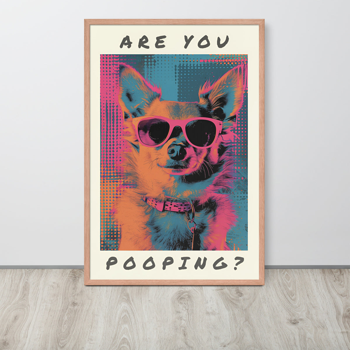 Chihuahua pop art poster leaning against a light wall on a wood floor. The poster shows a dog wearing sunglasses with the text 'ARE YOU POOPING?' in black lettering.