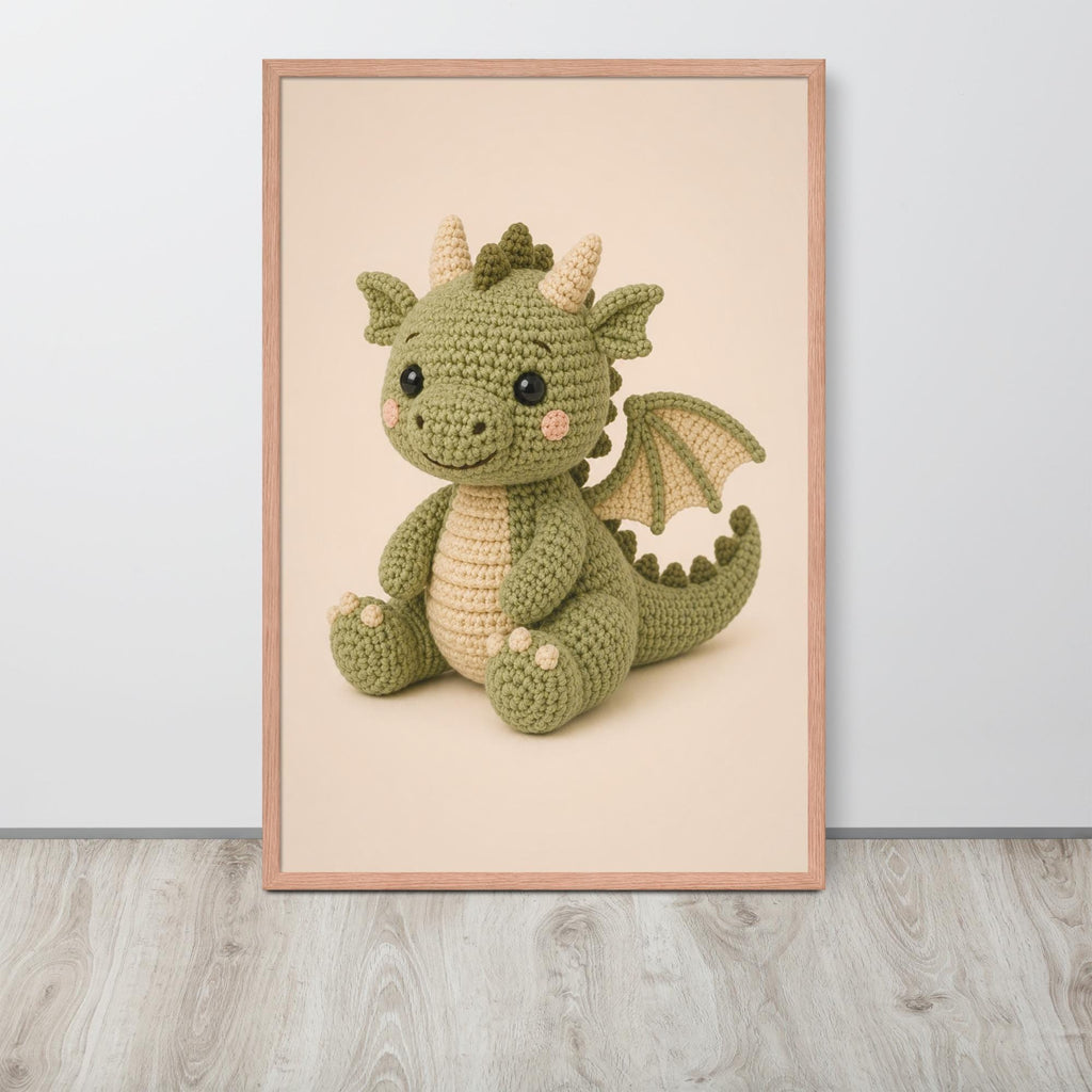 A framed fantasy nursery wall art print featuring a crocheted green dragon toy, displayed against a light gray wall on a light wood floor.