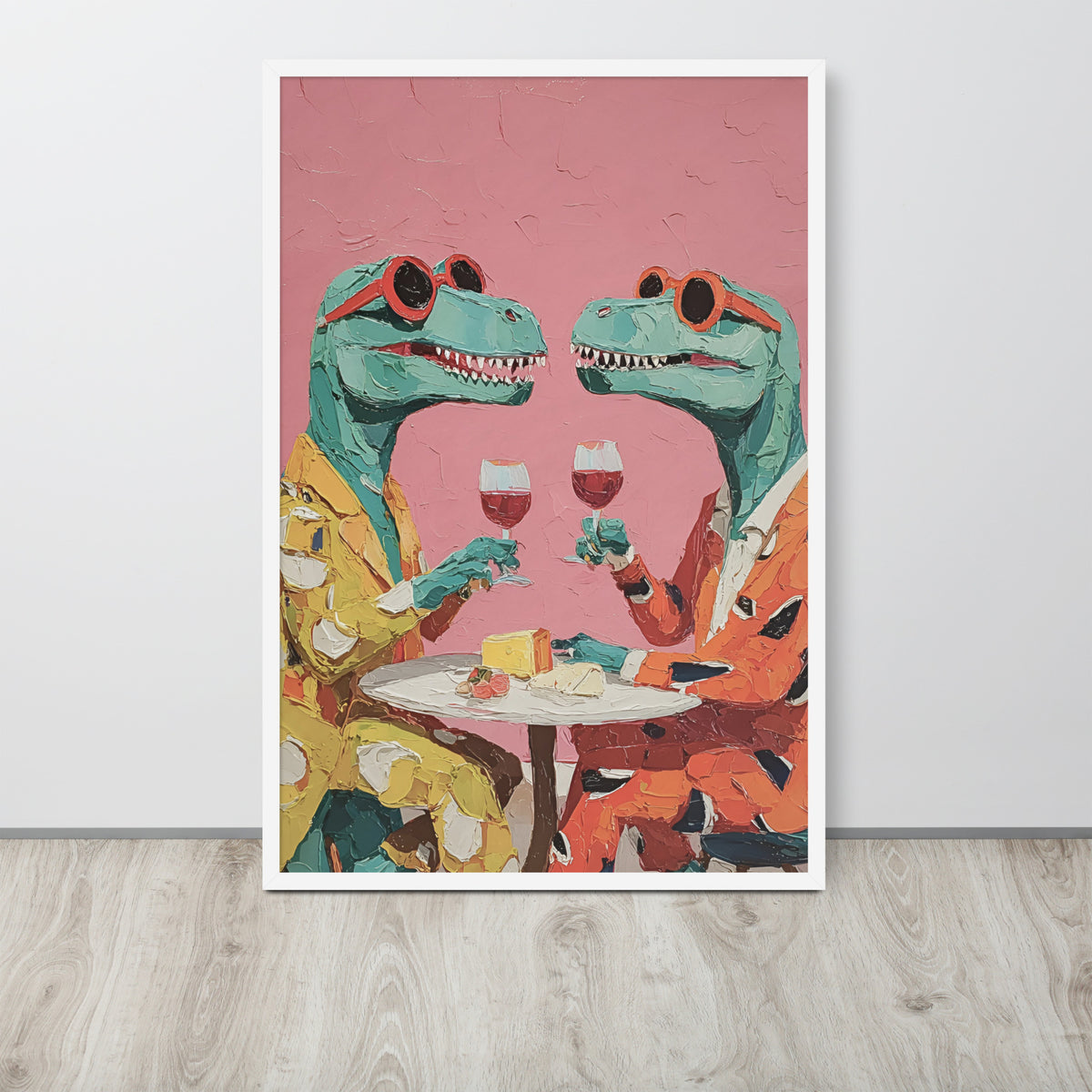 Funny kitchen art print featuring two cartoon dinosaurs wearing sunglasses and suits, sitting at a table with wine glasses and cheese on a pink background, displayed against a light gray wall on a light wood floor.