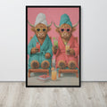 Funny bathroom wall art print featuring two Highland cows in colorful robes sitting on wooden chairs against a pink background, displayed on a light gray wall above a light wood floor.