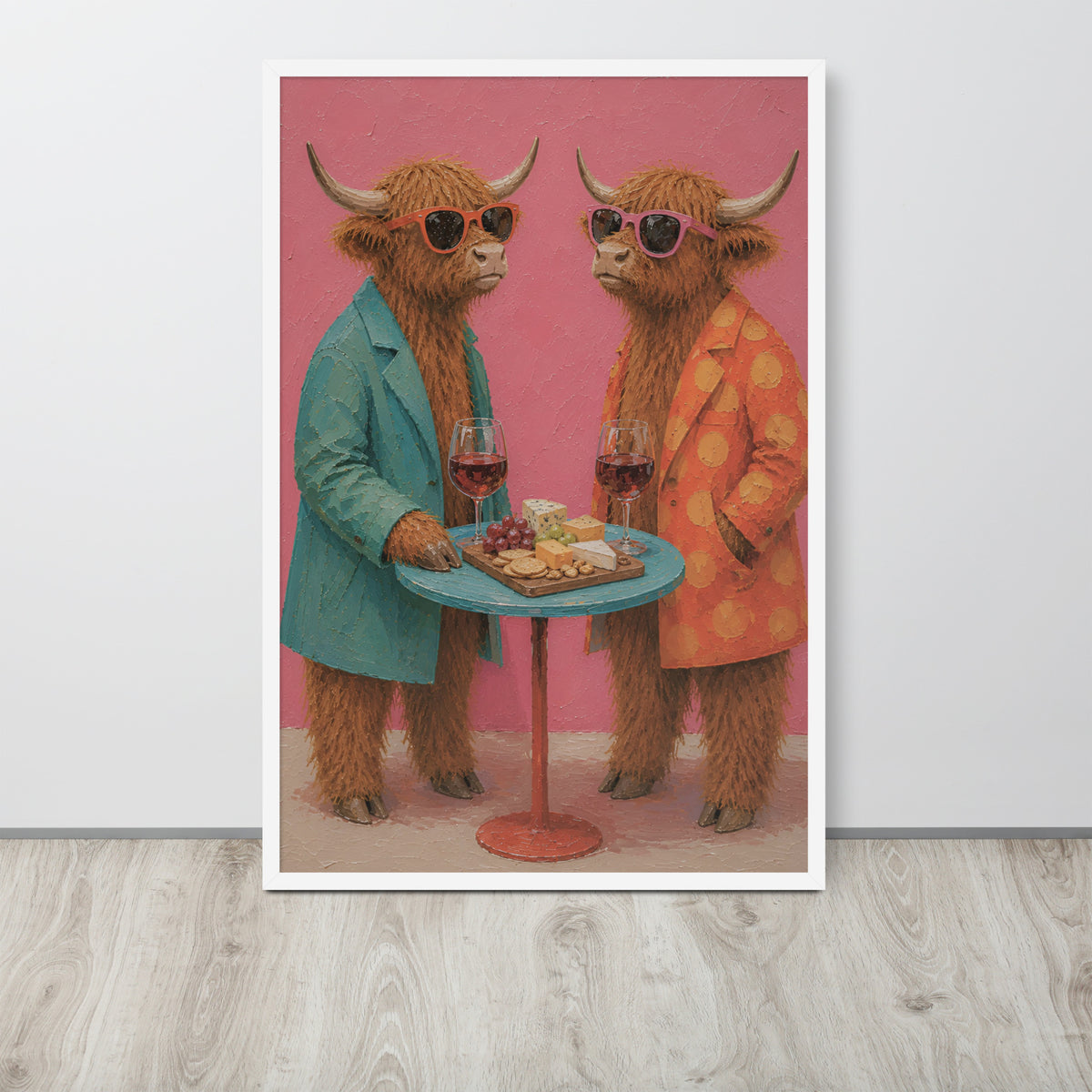 A framed funny farm wall art print featuring two fluffy Highland cattle in sunglasses, one in a teal blazer and one in an orange polka-dot jacket, standing behind a small table with wine glasses and cheese. The print is displayed against a light gray wall on a light wood floor.