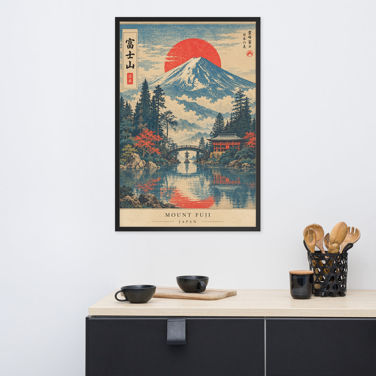 A framed Japanese-style art print of Mount Fuji hangs on a white wall above a light wood cabinet with black cups and utensils.