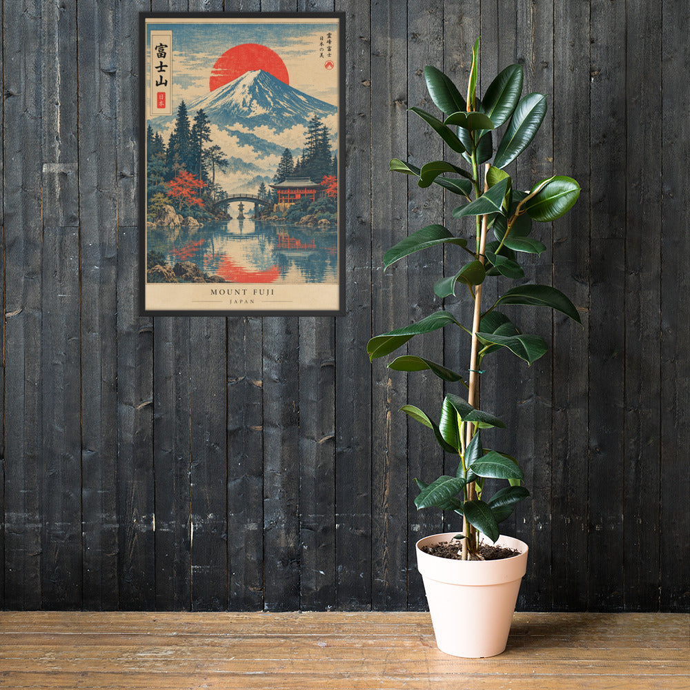 A potted rubber plant in a light pink pot stands on a wooden table against a dark wood-paneled wall, next to a framed Japanese art print of Mount Fuji.