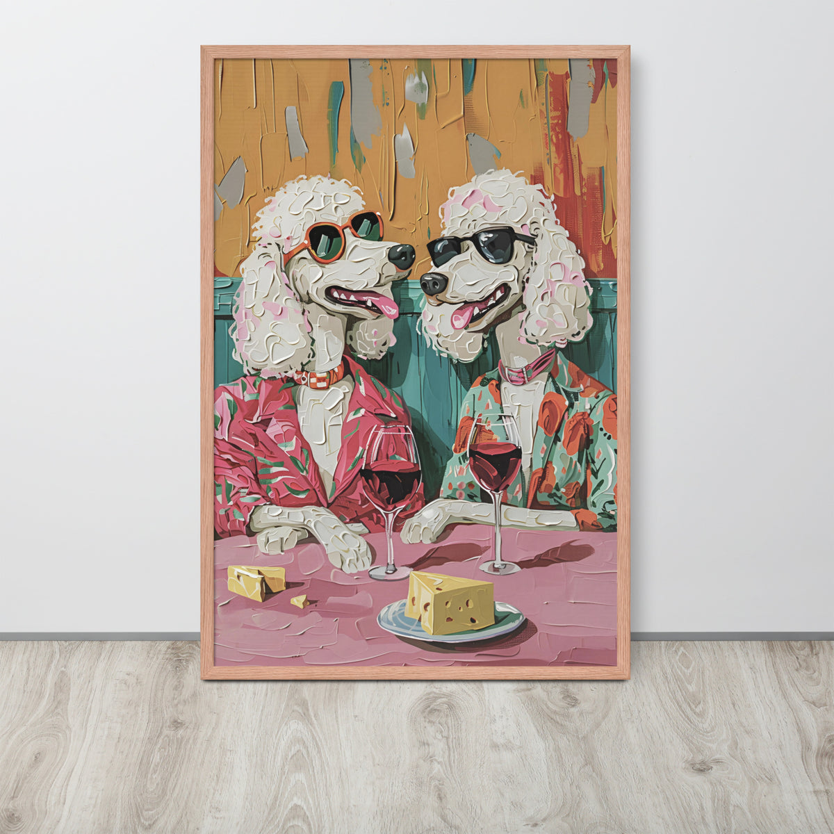 Funny kitchen wall art print depicting two poodles in stylish sunglasses and colourful suits sitting at a table with cheese and wine glasses, shown leaning against a white wall on a light wood floor.