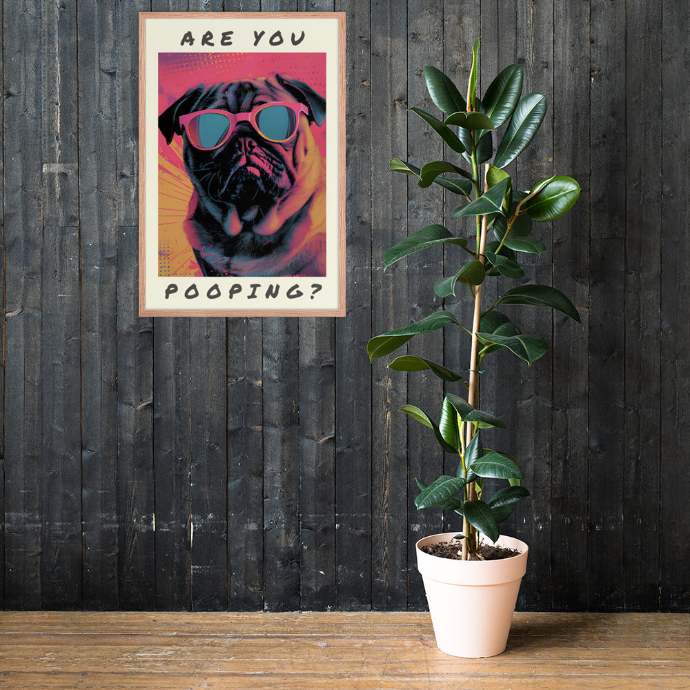 Toilet poster featuring a pop art pug wearing pink sunglasses with the text 'ARE YOU POOPING?' hanging on a dark wood wall, next to a potted green plant on a wooden table.