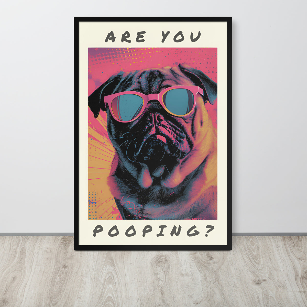 Pop art style washroom loo poster leaning against a light wall on a wood floor. The poster shows a pug wearing pink sunglasses with the text 'ARE YOU POOPING?' in black lettering on a cream background.