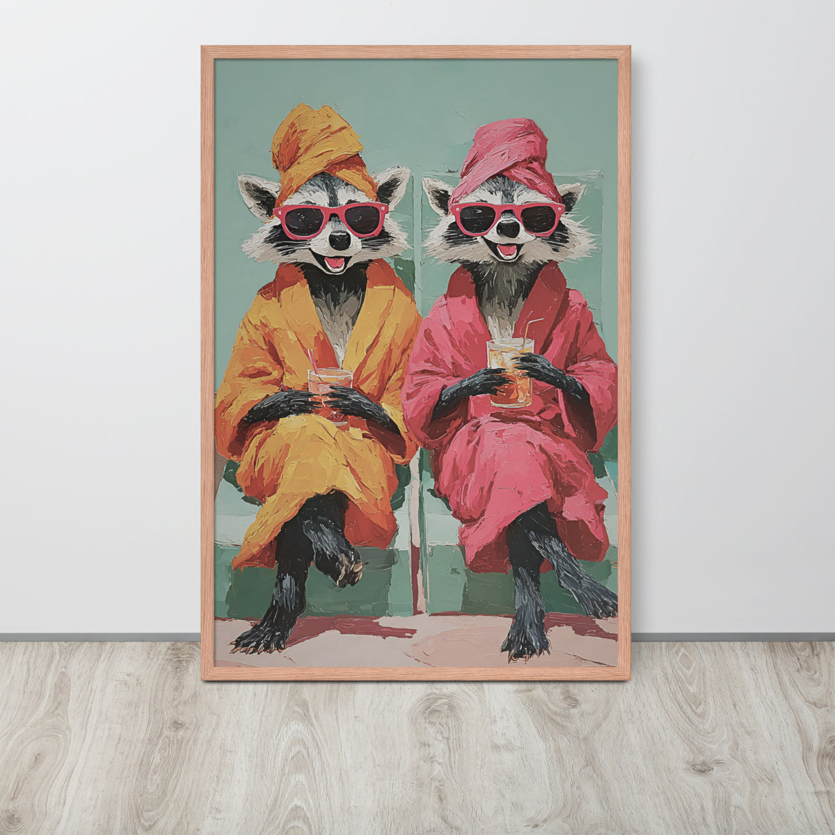 Raccoon bathroom wall art print featuring two cartoon-like raccoon animals wearing pink sunglasses and robes, one in orange and one in pink, sitting and holding drinks. The print is displayed leaning against a white wall on a light wood floor.