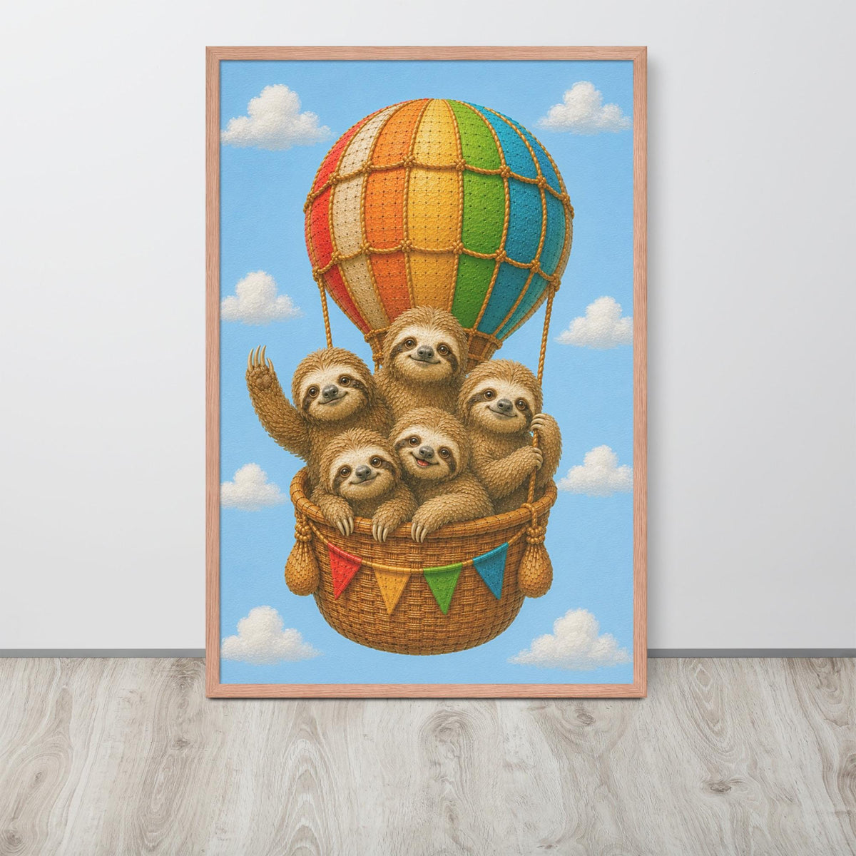 A framed nursery wall art print featuring five sloths in a wicker basket on a colorful striped hot air balloon against a blue sky with clouds, displayed on a light wood floor against a white wall.