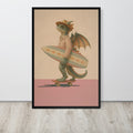 A framed vintage fantasy wall art print leaning against a white wall on a light wood floor. The print shows a green dragon wearing a hat and striped shirt, holding a surfboard while riding a skateboard, with a beige background and pink lower section.