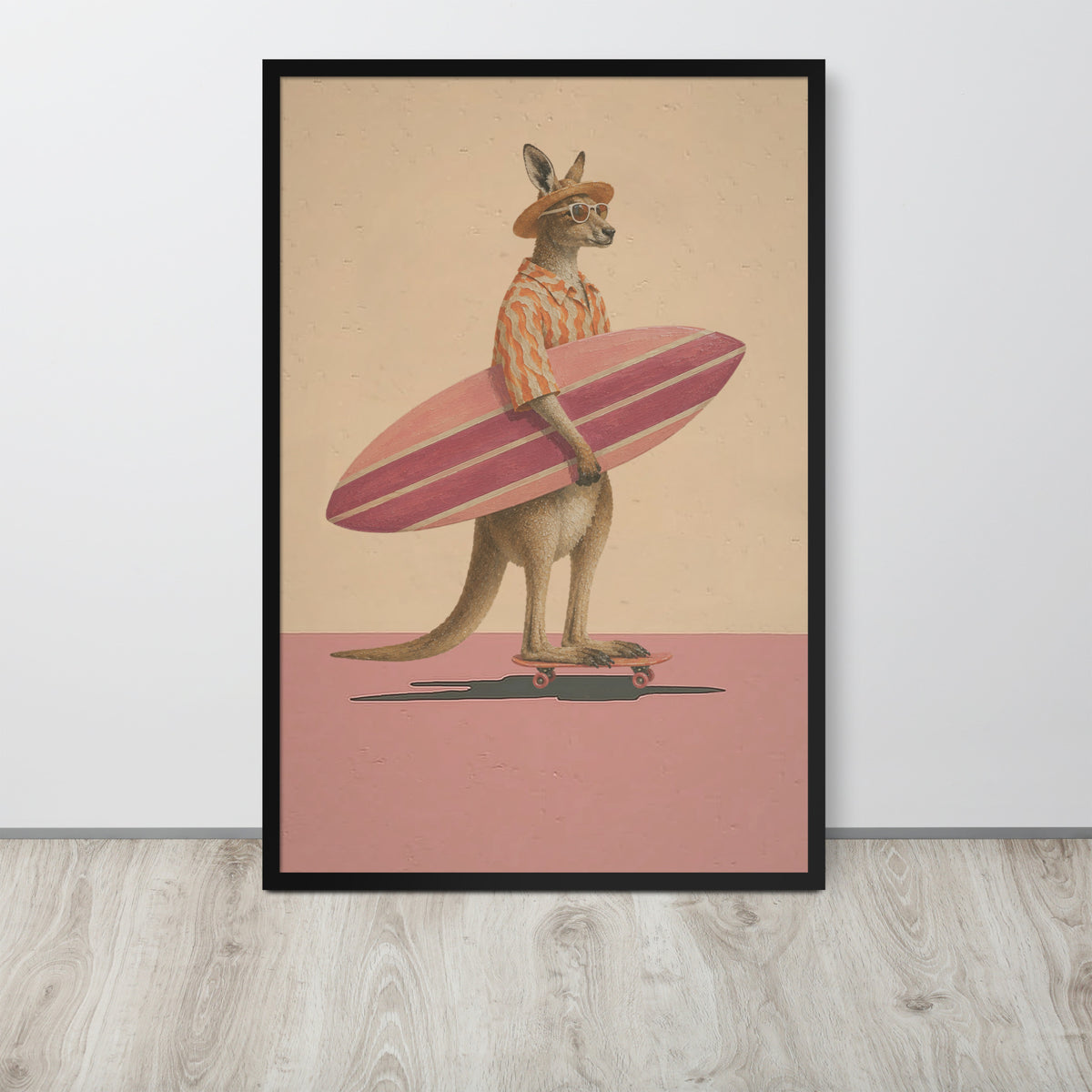 A framed Australian kangaroo wall art print featuring a kangaroo dressed as a surfer, holding a pink striped surfboard and wearing a striped shirt, standing on a skateboard against a beige and pink background. The print is displayed on a light gray wall above a light wood floor.