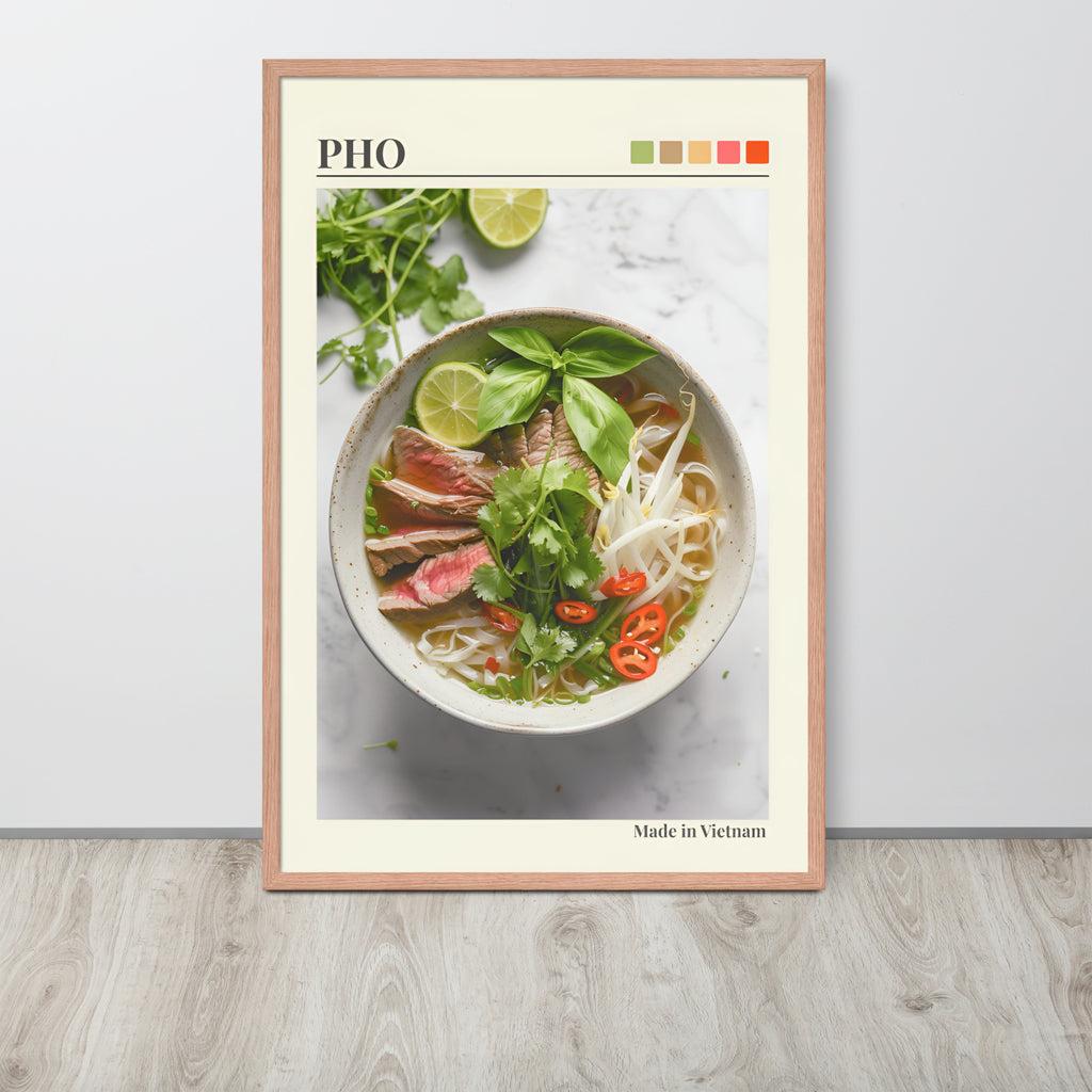 Pho Lover Decor wall art print leaning against a light wall on a wood floor, featuring a photograph of a bowl of pho noodle soup with herbs, lime, and sliced meat. The print has a cream border, the word PHO at the top, a small colour palette strip, and 'Made in Vietnam' at the bottom.