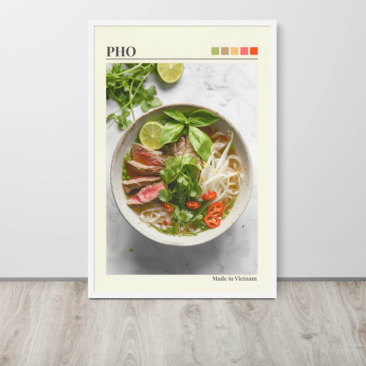 Vietnamese pho wall art print leaning against a light wall on a wood floor. The print features a photograph of a bowl of pho noodle soup with basil, lime, and red chilli, with the word 'PHO' at the top and 'Made in Vietnam' at the bottom.